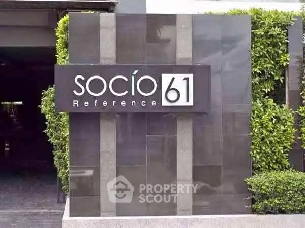 Modern building entrance with stylish signage and lush greenery, showcasing contemporary architectural design.
