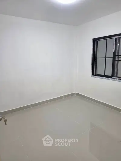 Spacious empty room with tiled floor and large window, perfect for customization.