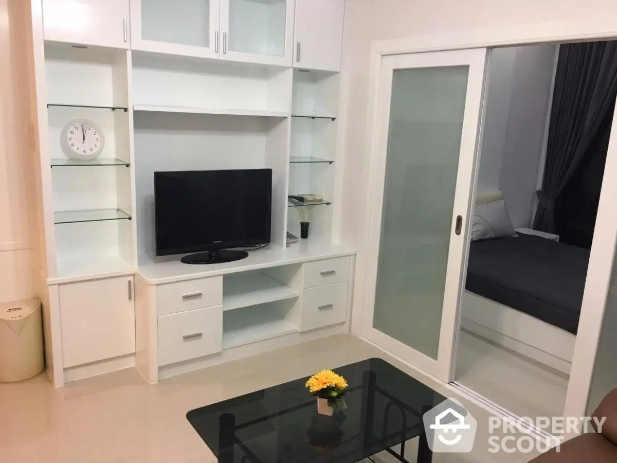 Cozy and modern living space featuring built-in white shelving units, sleek TV stand, and frosted glass doors leading to a serene bedroom.