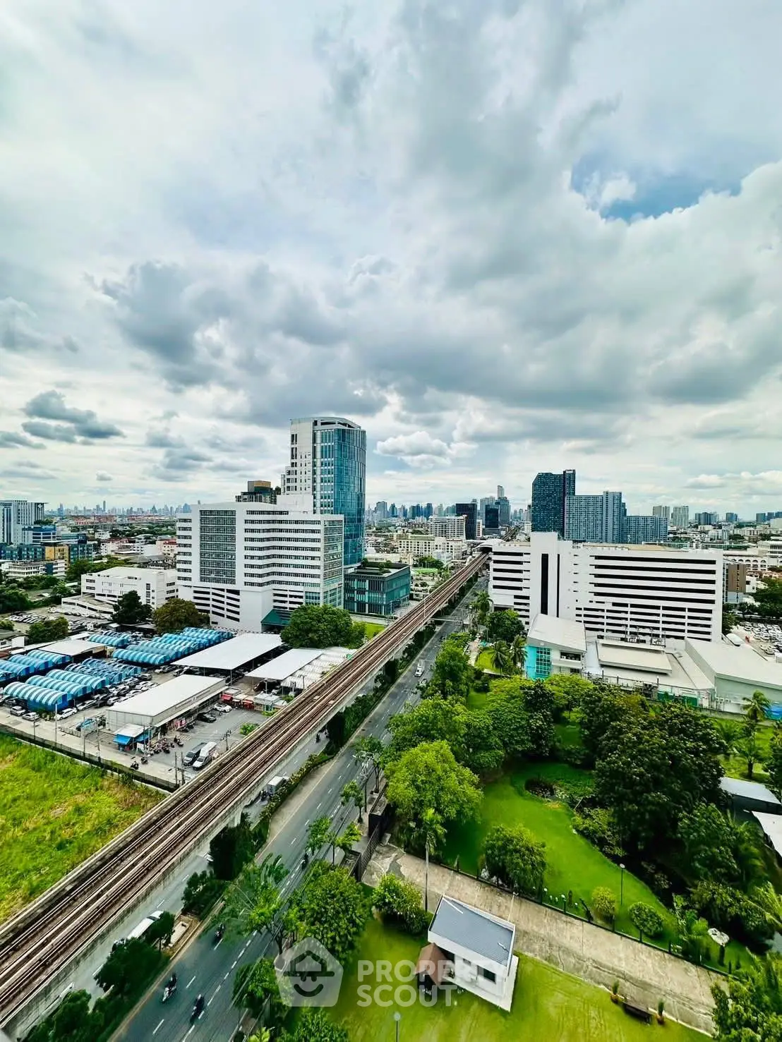 Stunning cityscape view with lush greenery and modern buildings under a cloudy sky.
