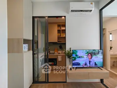 Modern living room with sleek kitchen and TV, featuring stylish decor and air conditioning.