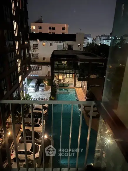 Night view of apartment complex with illuminated pool and parking area.