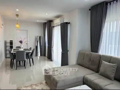 Modern living room with elegant gray sofa and dining area, featuring large windows and stylish curtains.