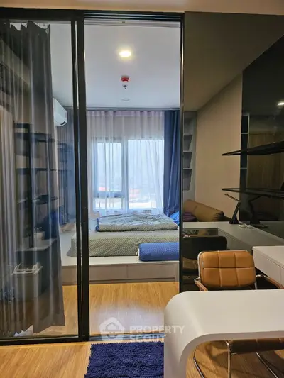 Modern studio apartment with glass partition, cozy bed, and stylish workspace.