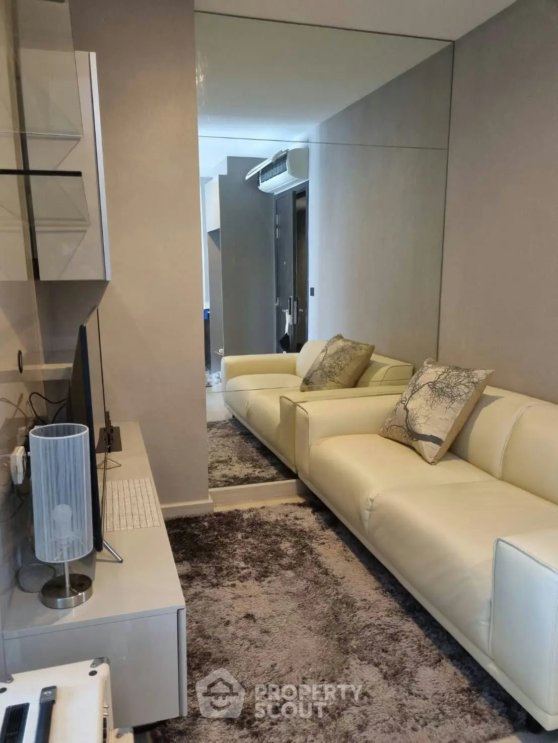 Modern living room with sleek design, featuring a plush white sofa, stylish decor, and a large mirror enhancing space.