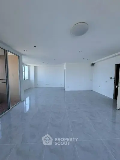 Spacious empty living room with modern tile flooring and large windows for natural light.