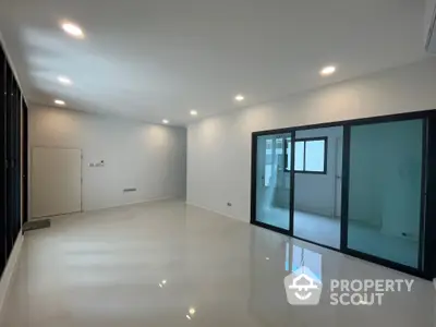 Spacious and modern living area with glossy white flooring, recessed lighting, and large glass doors leading to an adjacent room, perfect for contemporary living.