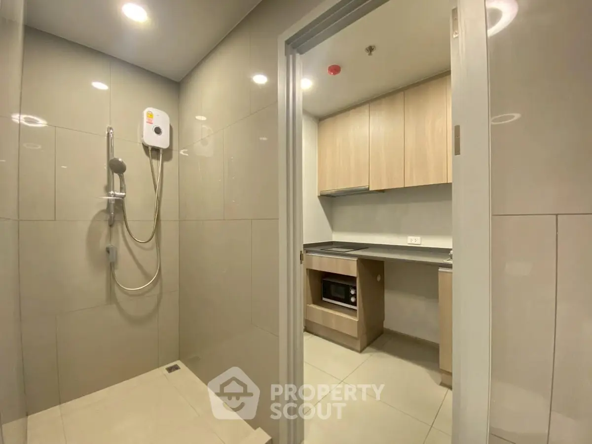 Modern bathroom with shower and adjacent compact kitchen in sleek apartment
