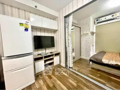 Modern apartment interior with fridge, TV, and cozy bedroom view.
