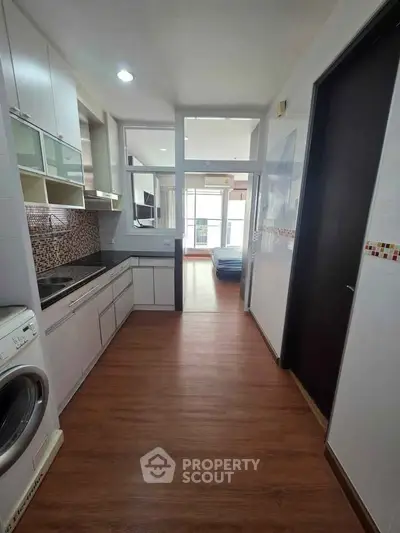 Modern kitchen with sleek cabinetry and washing machine, leading to a bright living area with large windows.