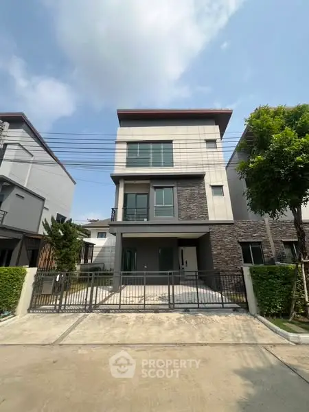 Modern three-story house with sleek design and gated driveway in suburban neighborhood.