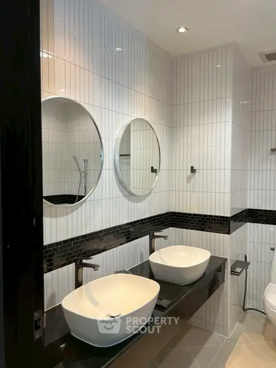 Modern bathroom with dual sinks and round mirrors, featuring sleek black and white tile design.