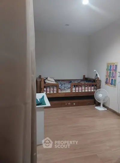 Cozy bedroom with wooden flooring, single bed, and fan, ideal for a comfortable living space.
