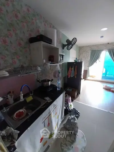Cozy kitchen with floral wallpaper and open layout leading to a bright living area with balcony.