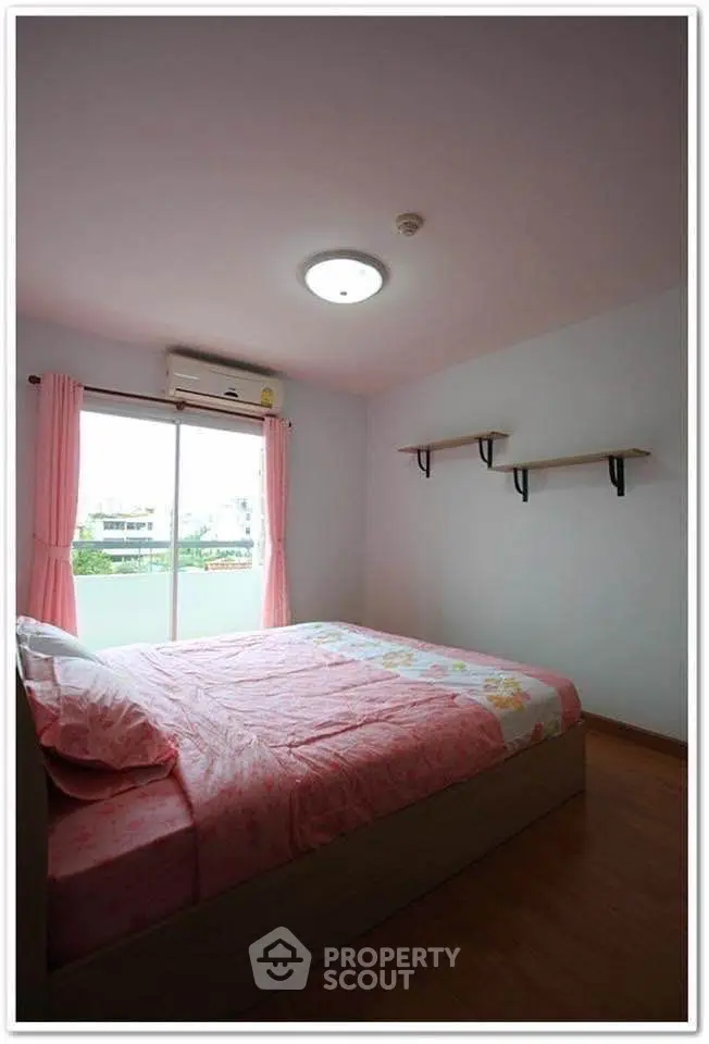 Cozy bedroom with pink decor and natural light from large window.