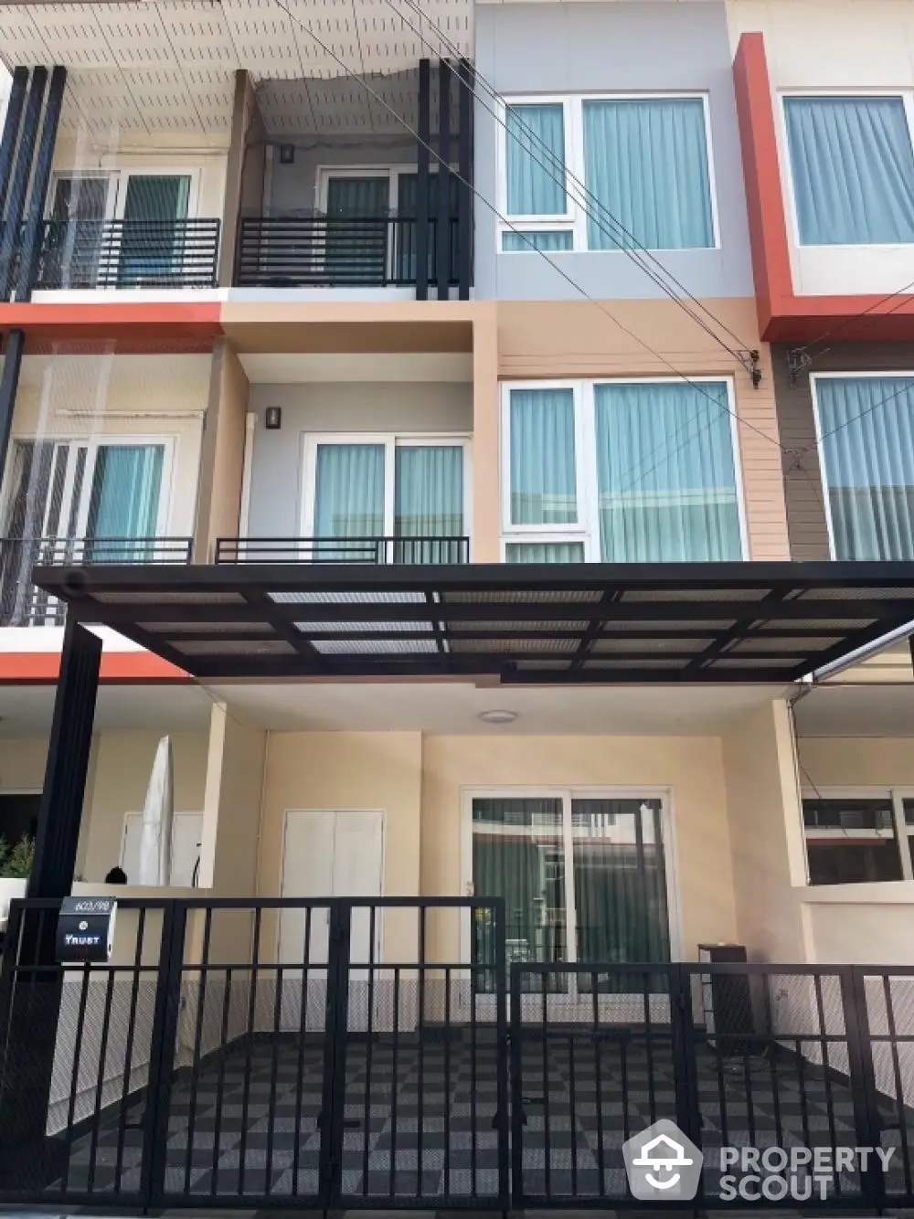 Modern townhouse with striking color accents, featuring a secure gated entrance and a shaded carport, ideal for urban living.