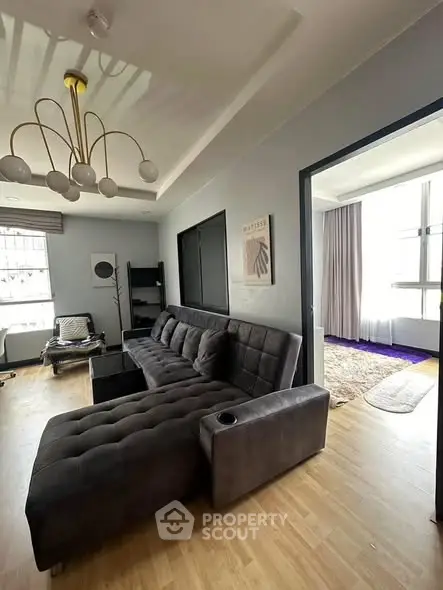 Modern living room with stylish gray sectional sofa and elegant lighting, featuring large windows for natural light.