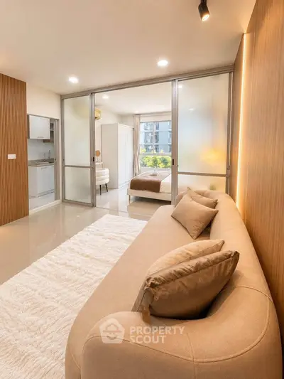 Modern living room with cozy beige sofa and view into stylish bedroom through sliding glass doors.