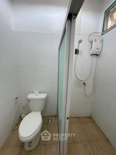 Modern bathroom with shower and toilet in a compact layout, featuring white tiles and a sleek design.