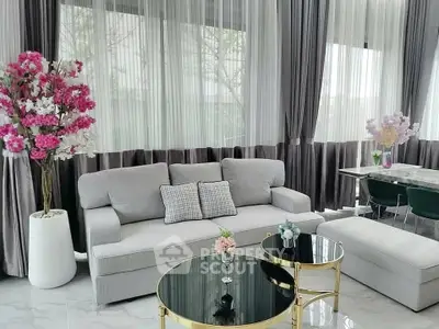 Elegant living room with plush gray sofa, chic coffee tables, and floor-to-ceiling windows with sheer curtains.