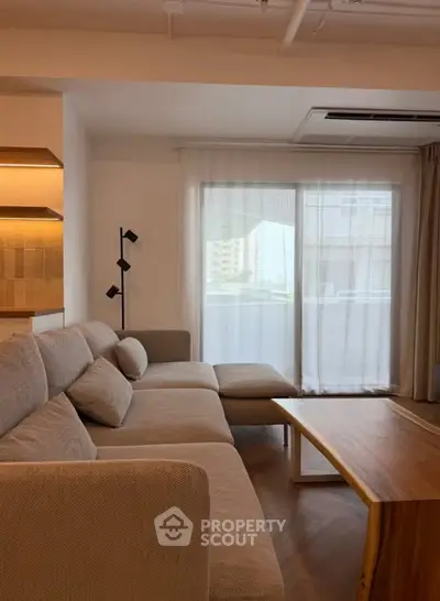 Modern living room with cozy sectional sofa and wooden coffee table, featuring large window with city view.