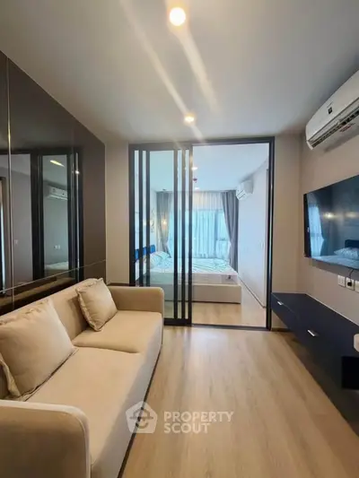 Modern living room with glass partition leading to a cozy bedroom, featuring sleek design and natural light.