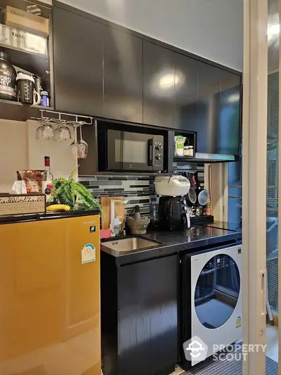 Compact modern kitchen with yellow fridge, microwave, and washing machine in stylish apartment.