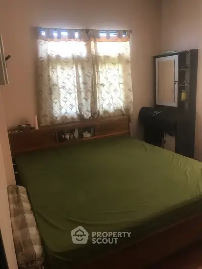 Cozy bedroom with green bedding and natural light through patterned curtains.