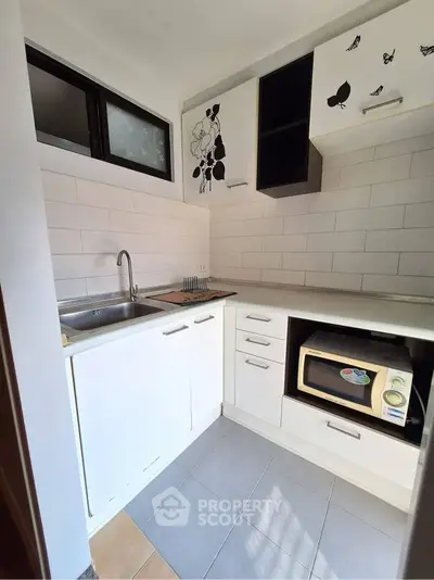 Compact kitchen with modern white cabinets and microwave, ideal for efficient cooking.