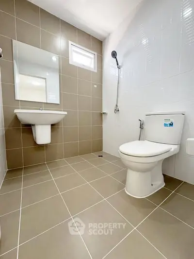 Modern bathroom with sleek fixtures and neutral tiles, featuring a shower and toilet.