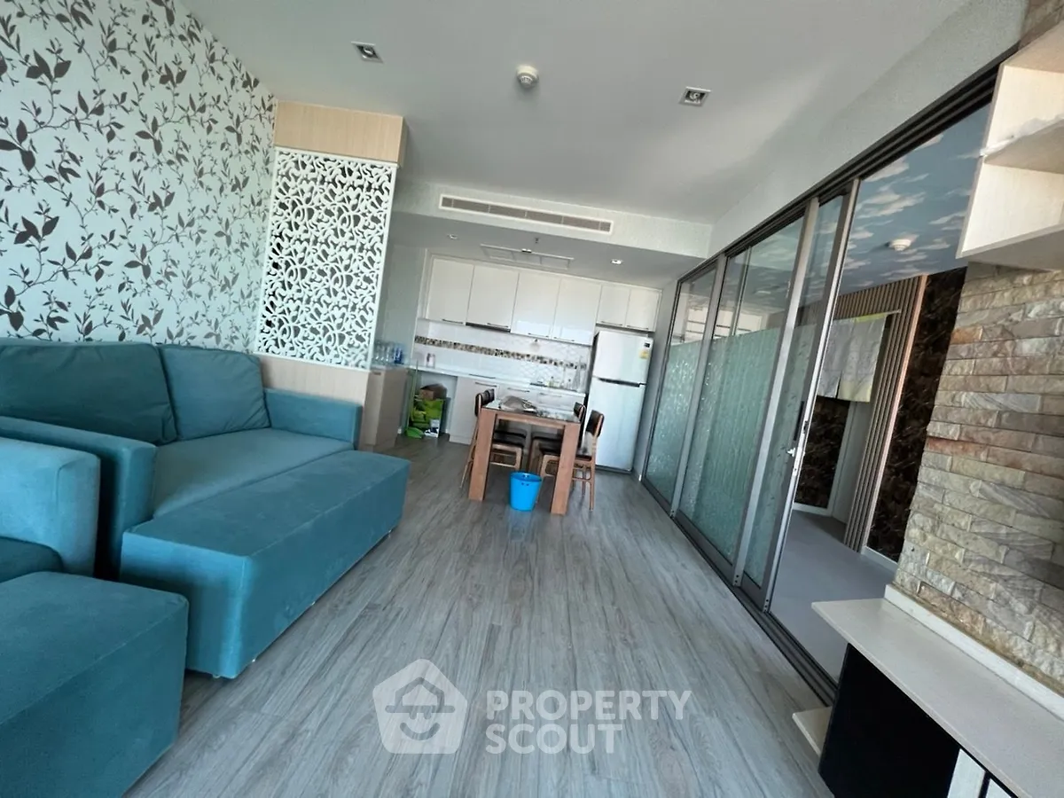 Modern living room with teal sofa and open kitchen layout, featuring stylish decor and ample natural light.