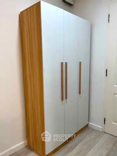 Modern wooden wardrobe in a minimalist bedroom corner with white walls and door.