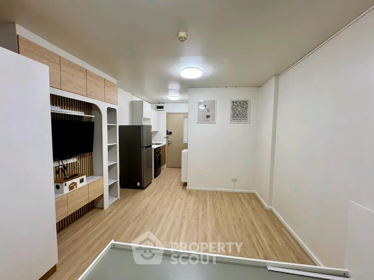 Modern open-plan living room with sleek kitchen and wooden flooring, featuring built-in storage and appliances.