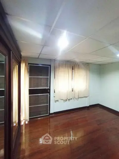 Spacious empty room with wooden flooring and large windows, perfect for customization.