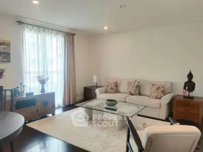 Elegant living room with cozy sofa, glass coffee table, and natural light from large window.