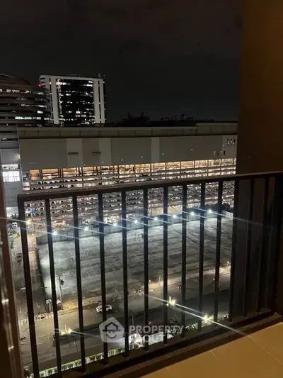 Night view from balcony overlooking cityscape and illuminated parking structure.