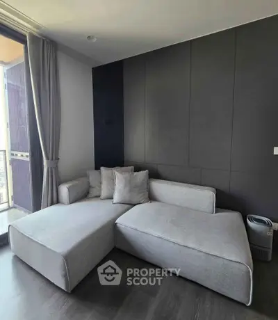 Modern living room with sleek gray sectional sofa and floor-to-ceiling windows offering city views.