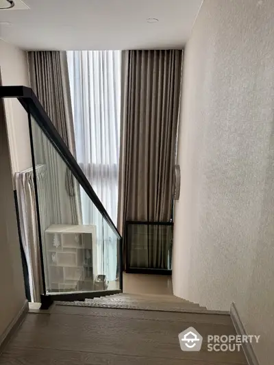 Modern staircase with glass railing and tall curtains in elegant home interior