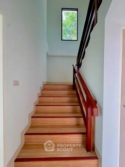 Elegant staircase with wooden railing and large window offering natural light