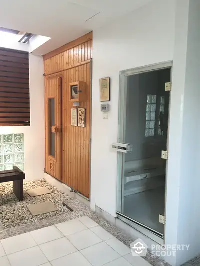 Inviting entrance area with a wooden door and modern glass door, complemented by natural light and a pebbled walkway, perfect for a welcoming home atmosphere.