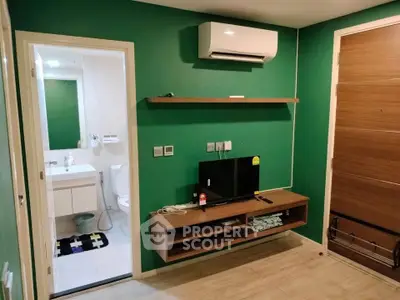 Modern living room with green walls, wall-mounted TV, and view into a stylish bathroom.