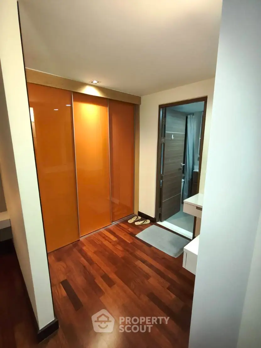 Modern apartment hallway with wooden flooring and orange sliding closet doors.