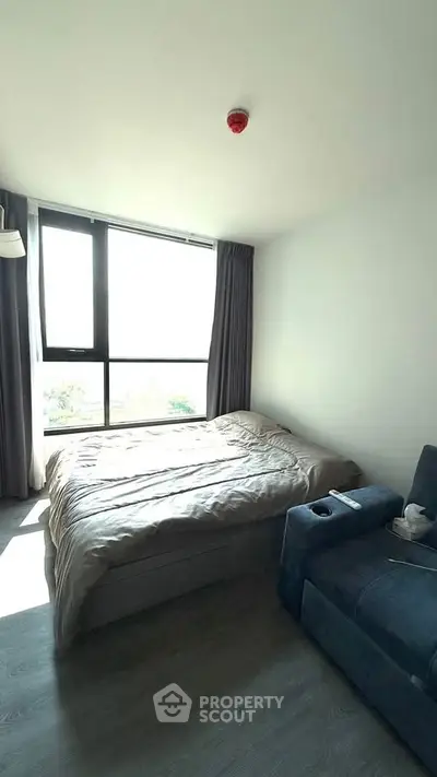 Cozy bedroom with large window and modern furnishings, offering ample natural light and a comfortable atmosphere.