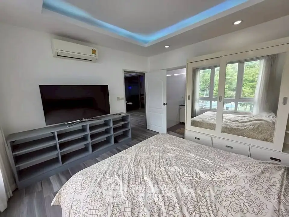 Modern bedroom with large TV and mirrored wardrobe, featuring elegant decor and natural light.