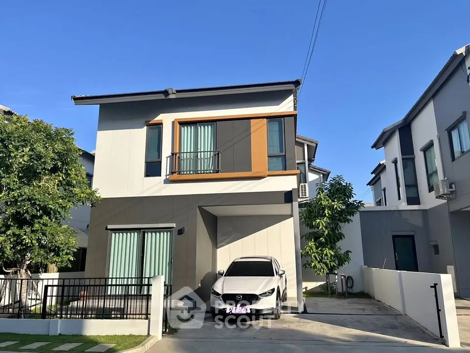 Modern two-story house with car parked in driveway, featuring sleek design and lush greenery.
