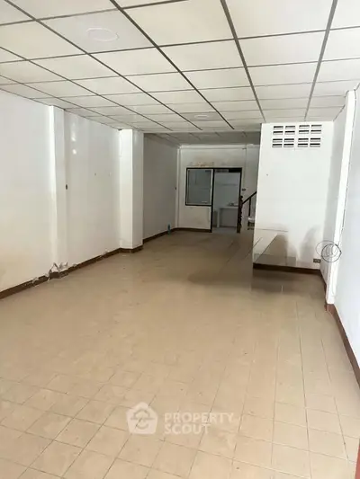 Spacious empty room with tiled floor and ceiling grid, ideal for customization.