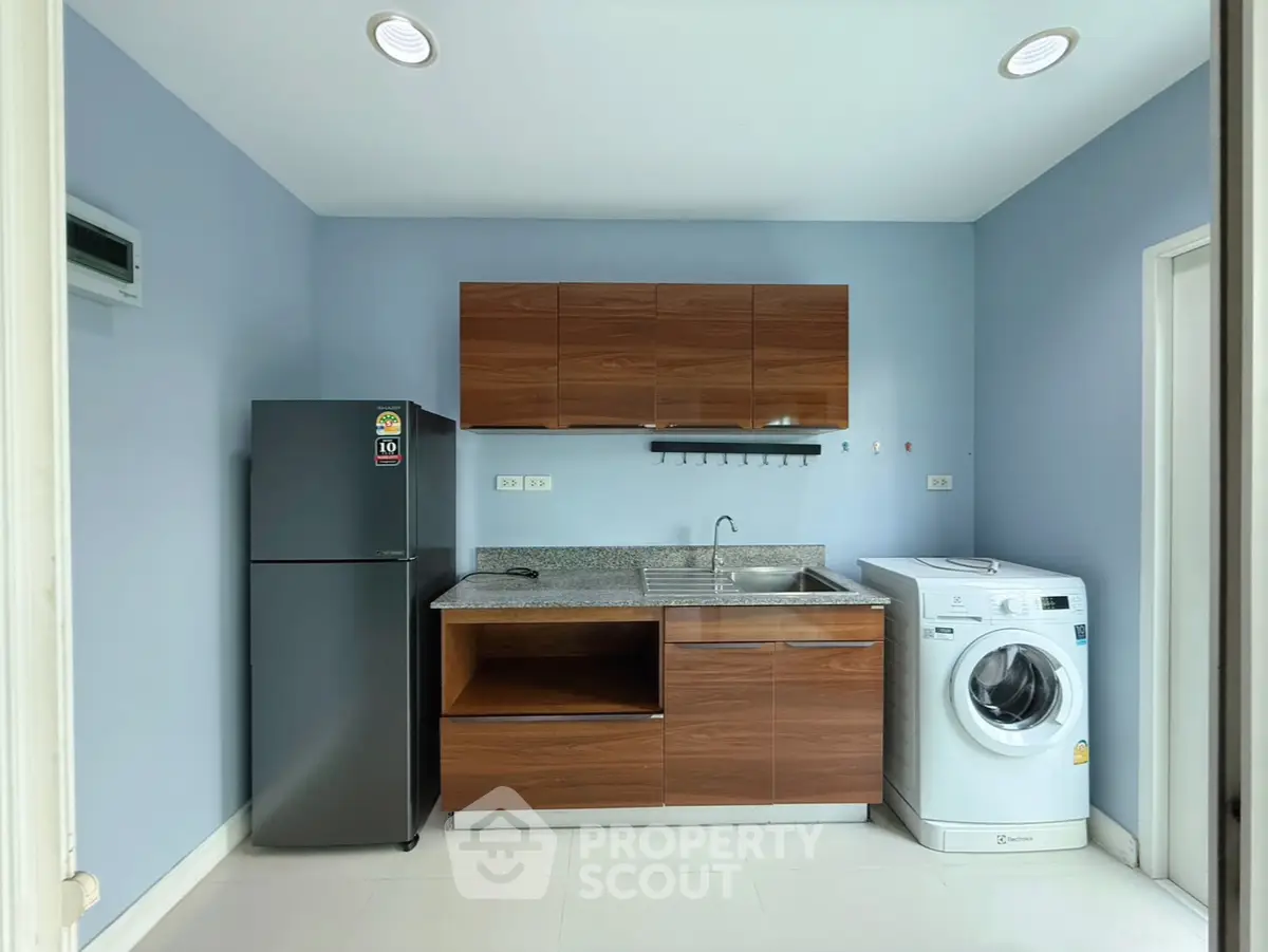 Modern kitchen with sleek cabinets, fridge, and washing machine in a compact layout.