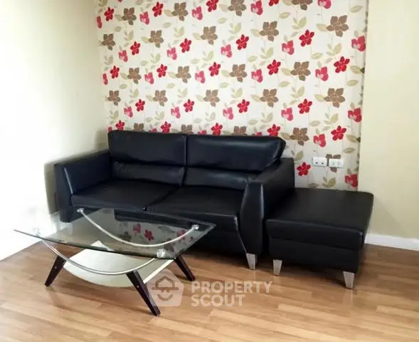 Stylish living room with black leather sofa and glass coffee table on wooden floor.