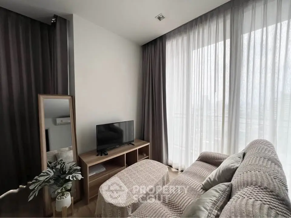 Cozy living room with modern decor, featuring a plush sofa, TV stand, and large window with sheer curtains.