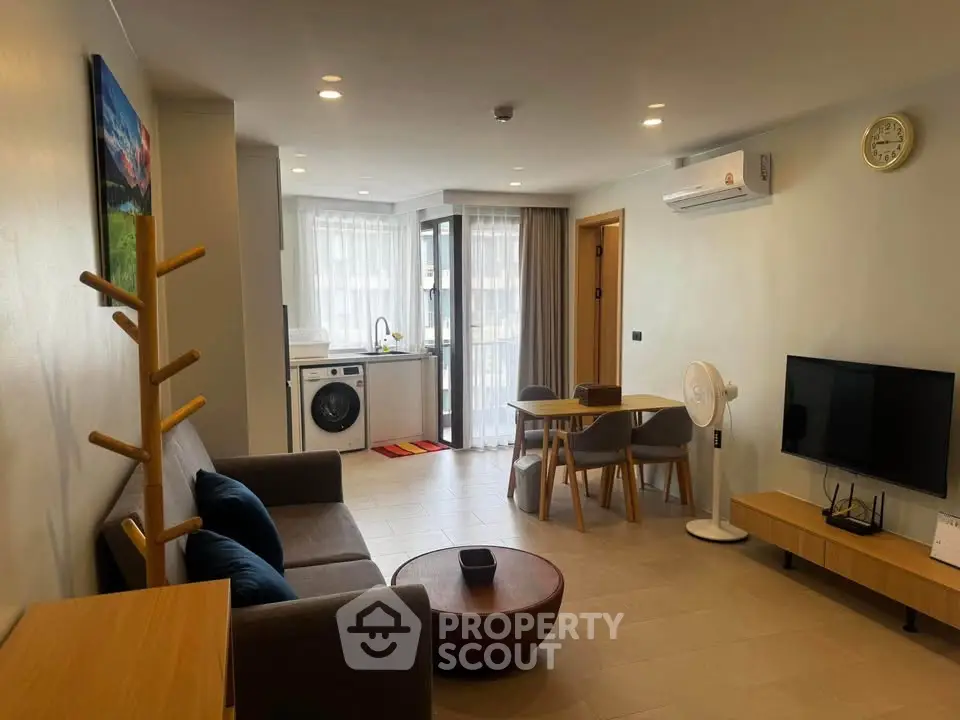 Modern living room with stylish furniture and open kitchen layout, featuring a washing machine and air conditioning.